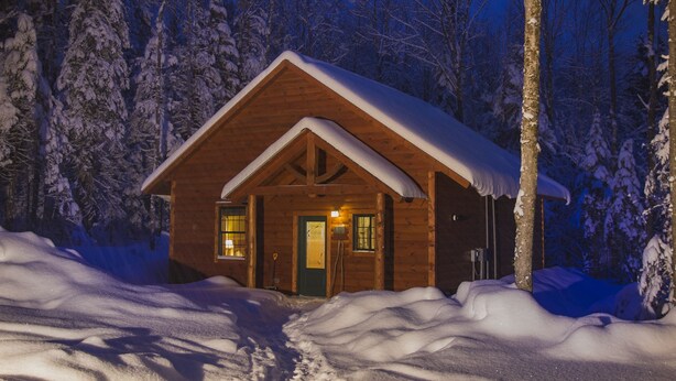 A wooden cabin with a snow-covered roof, surrounded by trees and snow. - Robert Frost Mountain Cabins (Ripton)