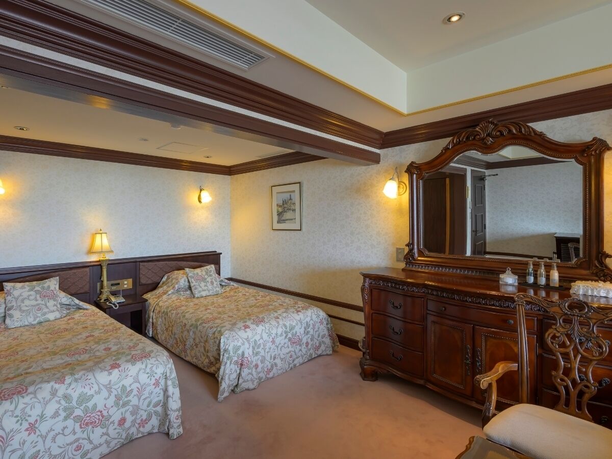 A hotel room with two beds, a dresser, a mirror, and wall sconces.