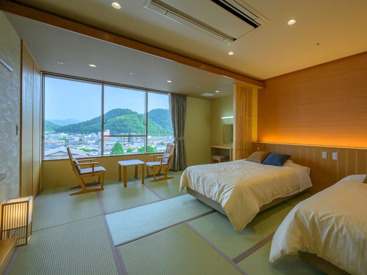 A hotel room with two beds, a view of a cityscape, a wooden desk, and a chair.
