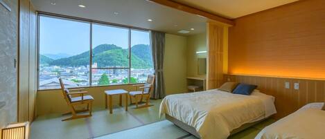 A hotel room with two beds, a view of a cityscape, a wooden desk, and a chair.