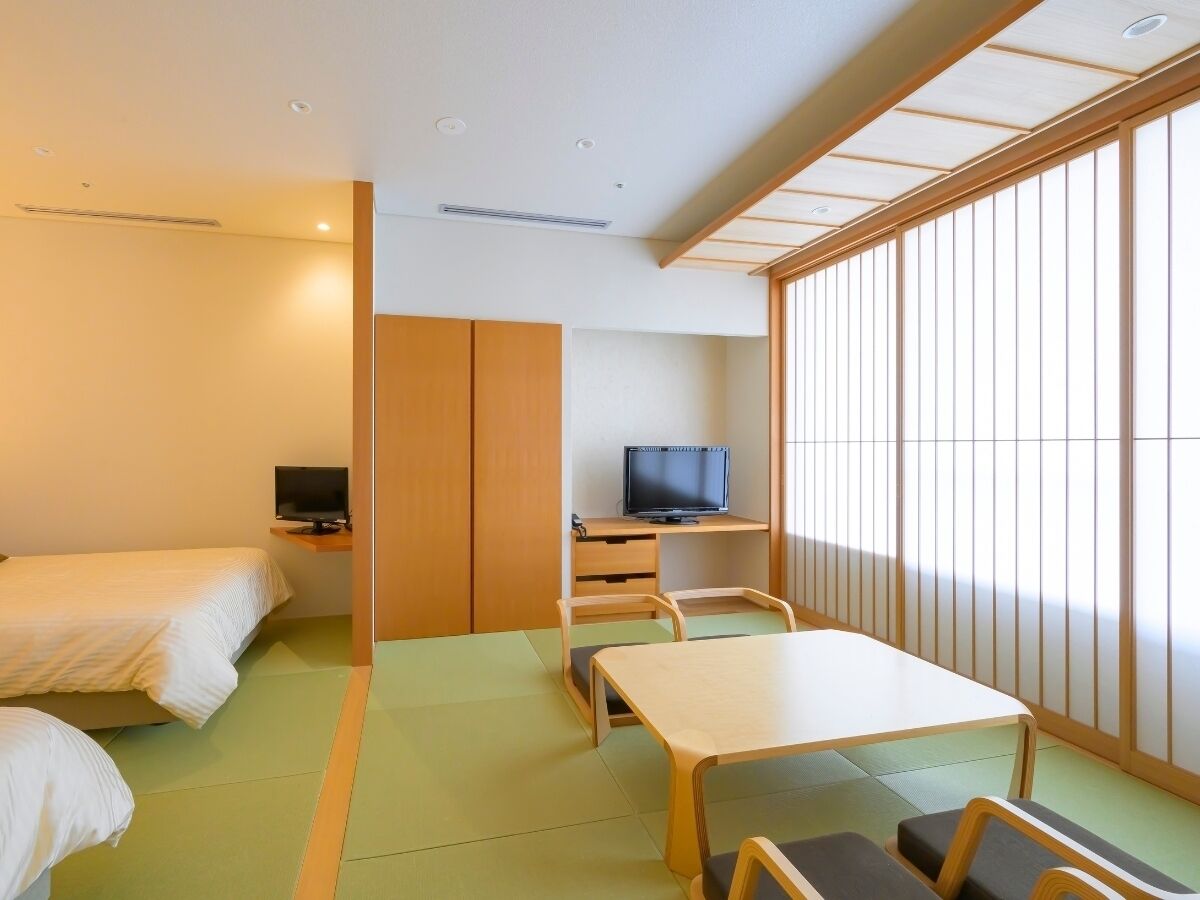 Habitación de hotel con dos camas, televisión, escritorio y piso de esteras de tatami.