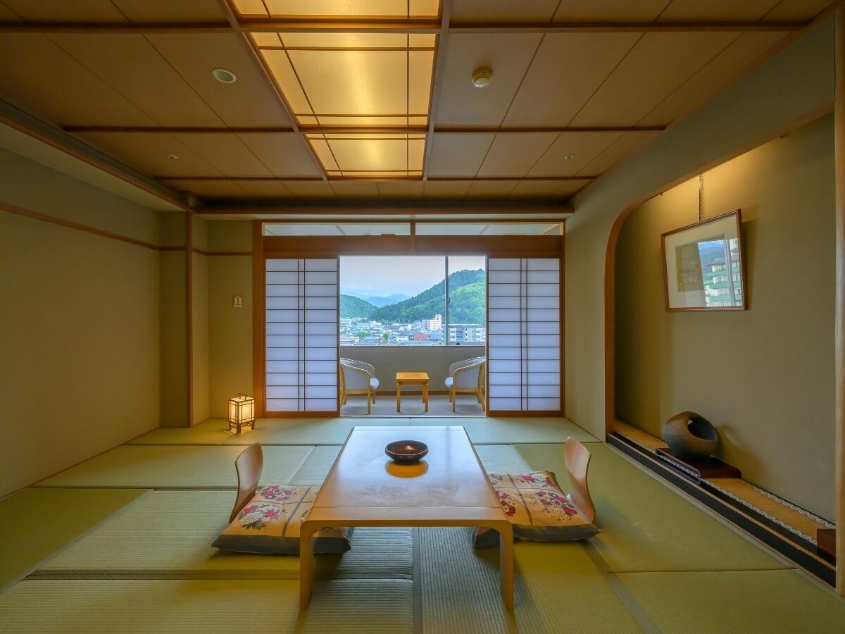 A traditional Japanese room with tatami flooring, a low table with a bowl, and a view of a mountain through large windows.