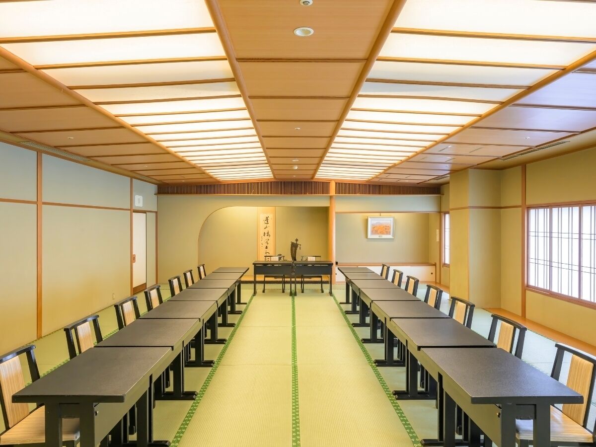 A conference room with long tables and chairs, a green mat on the floor, and a traditional Japanese aesthetic with tatami mats and shoji screens.