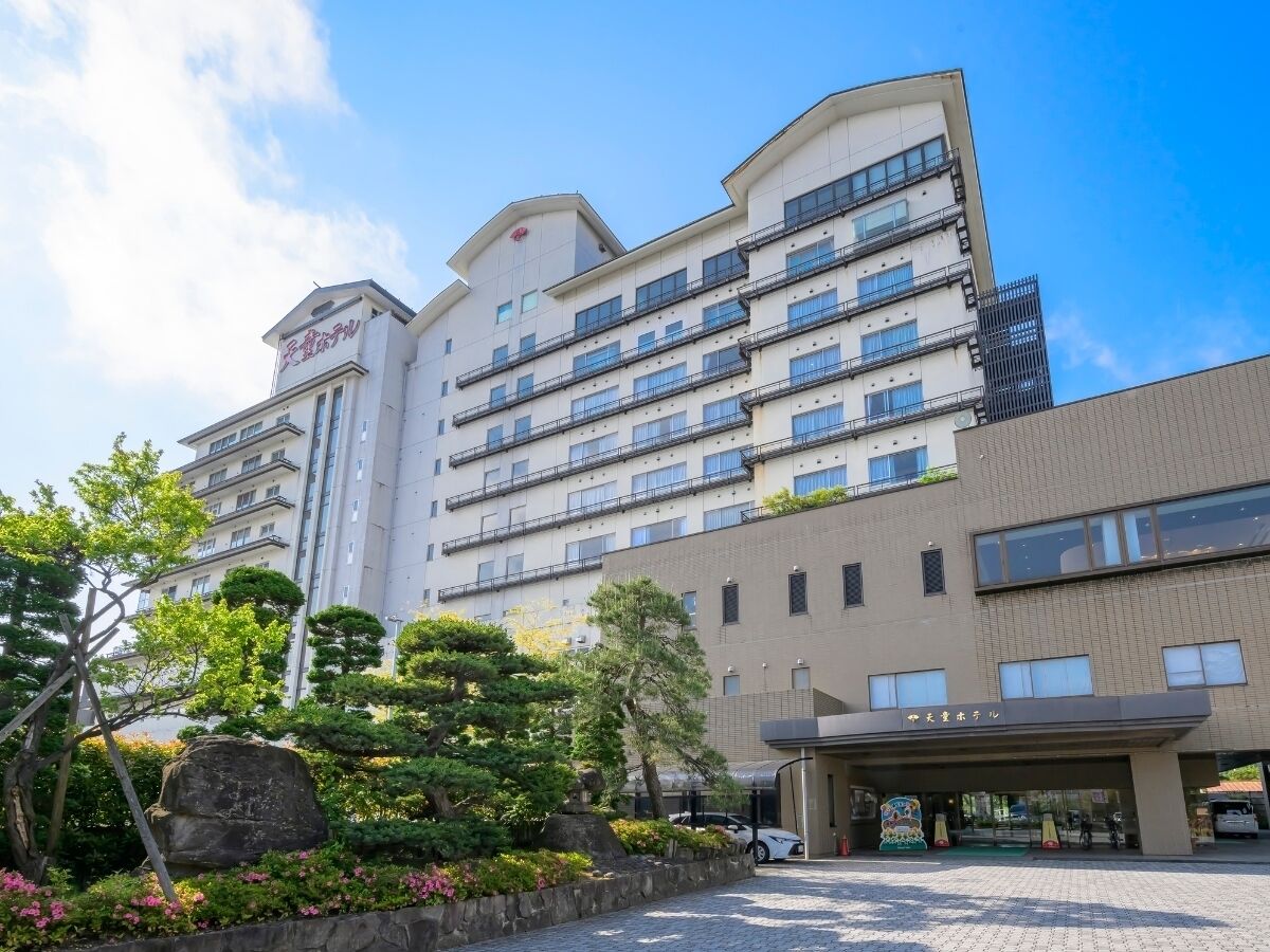 Un hotel de varios pisos con un diseño moderno, que cuenta con una entrada destacada y un área ajardinada con árboles y arbustos.