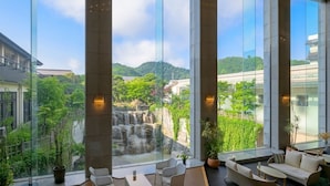 Habitación de hotel moderna con ventanas amplias que ofrecen vistas a una cascada y abundante vegetación.