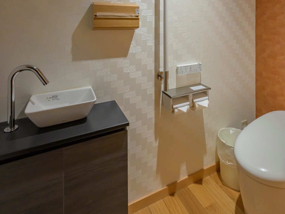 A bathroom with a white sink, a toilet, and a paper towel dispenser.