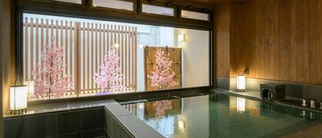 Piscina interior moderna con techo y paredes de madera, suelo de baldosas y vistas a flores de cerezo a través de un ventanal.