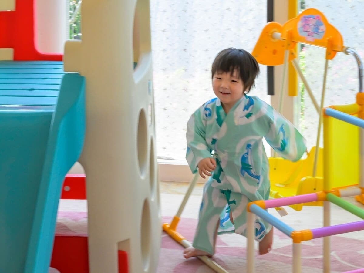 A child in a play area with colorful structures and a window in the background.