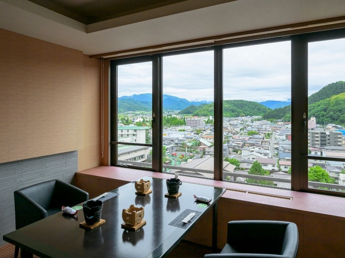 A room with a large window offering a view of a city and mountains. There is a table with a few items on it and two chairs.
