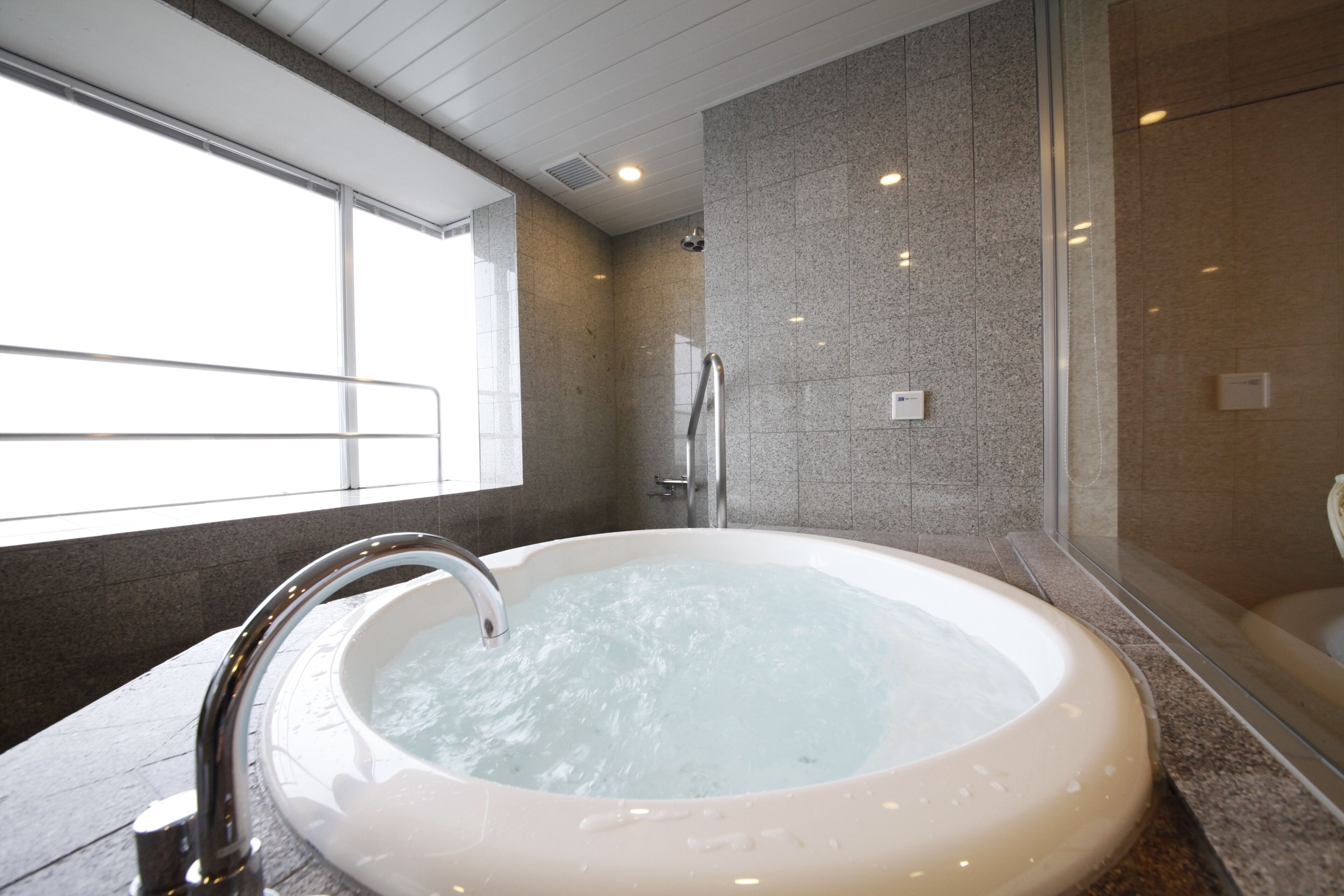 A modern bathroom with a large bathtub, a shower area, and a glass-enclosed window.