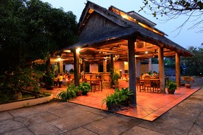 A thatched-roof outdoor dining area with stone flooring and potted plants. - Mea Culpa Kampot (Kampot)