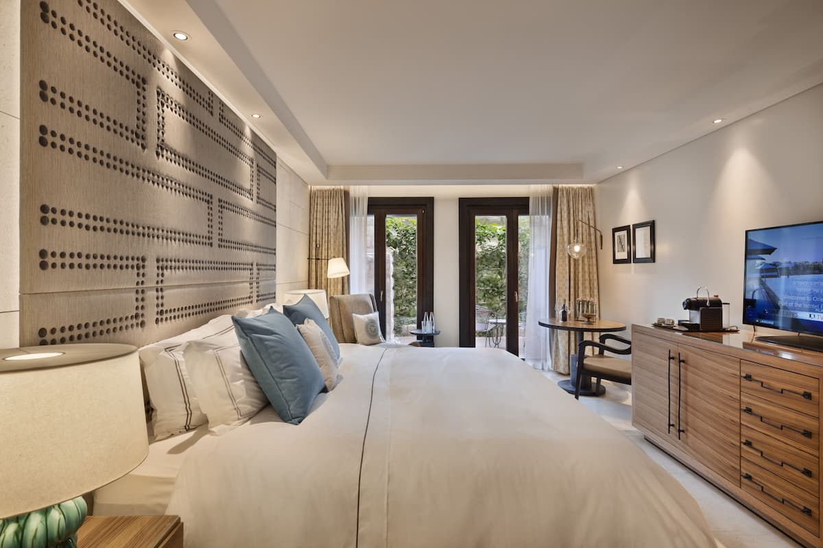 Una habitación de hotel moderna con una cama grande, televisor, cabecera de madera, escritorio y vistas al exterior.