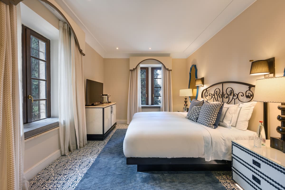 Un espacioso dormitorio con una cama grande, una mesita de noche, un aparador y una ventana con cortinas.
