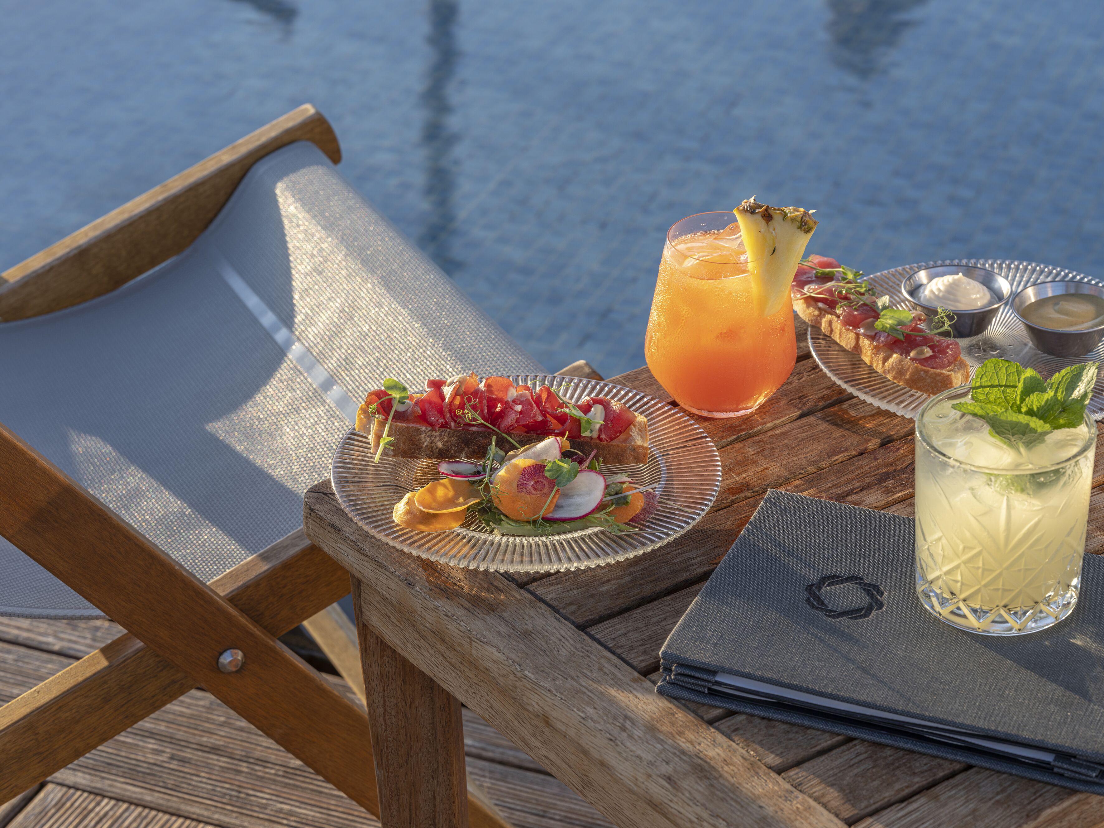A wooden table with a laptop, a glass of iced drink, and plates of food.