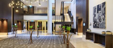 A spacious lobby with a geometric patterned floor, modern chandeliers, and a large artwork on the wall.