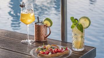 Ein Tisch mit einem Glas gelbes Getränk, einem Kupferbecher, einem hohen Glas mit Limettenscheibe und einem Teller mit Essen.