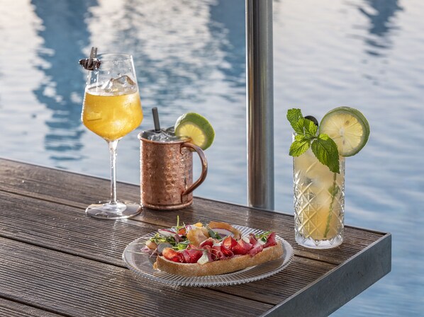 A table with a glass of yellow drink, a copper mug, a tall glass with a lime slice, and a plate of food. - Orient by Isrotel exclusive (Jerusalem)