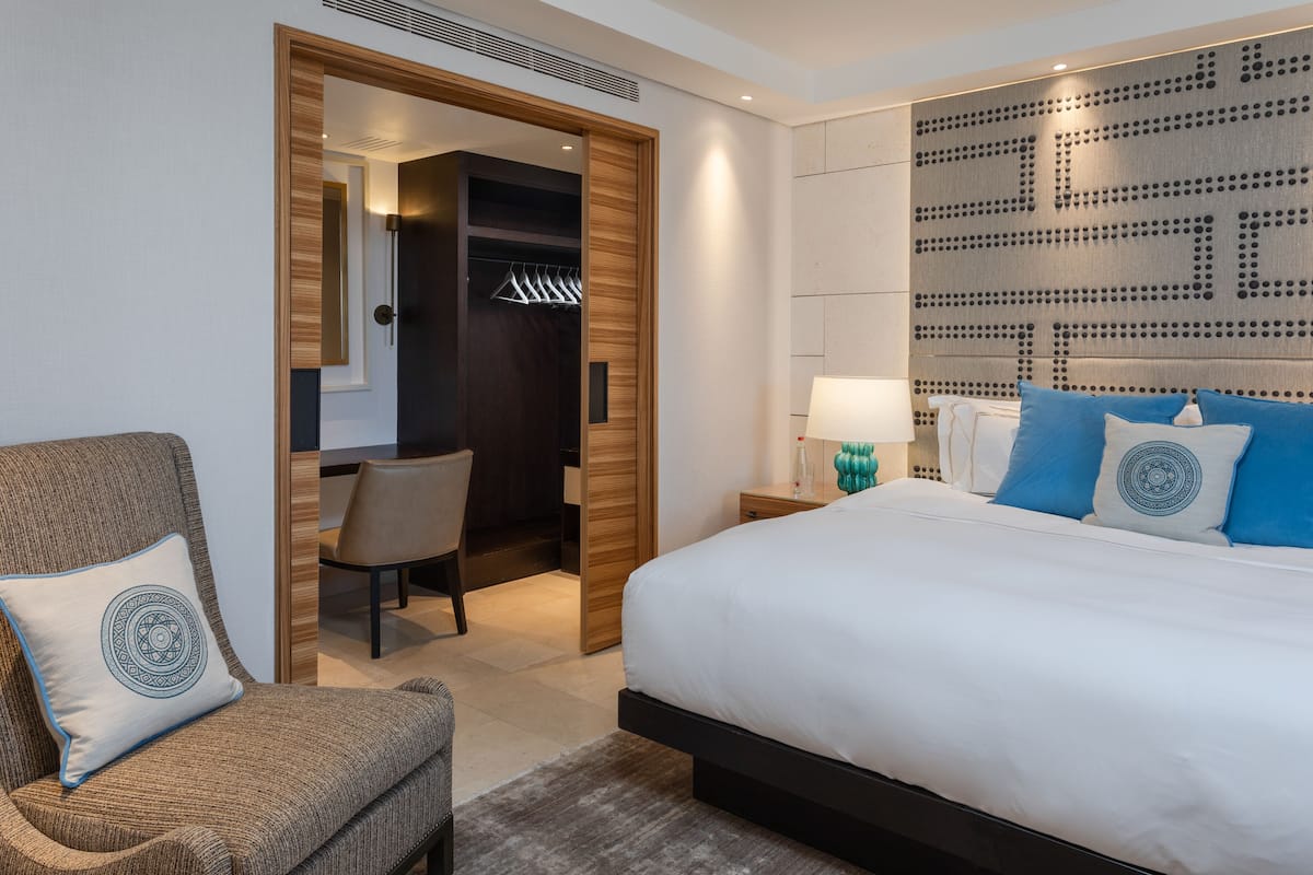 Una habitación de hotel moderna con una cama grande, una zona de estar con una silla, un vestidor y un panel decorativo en la pared.