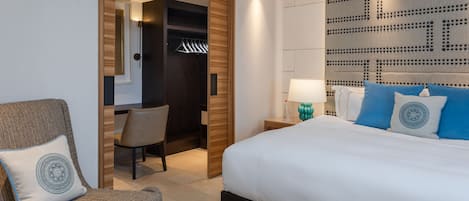 A modern hotel room with a large bed, a seating area with a chair, a walk-in closet, and a decorative wall panel.