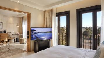 Habitación de hotel con cama, televisión, balcón con vista a la ciudad y zona de comedor con mesa y sillas.