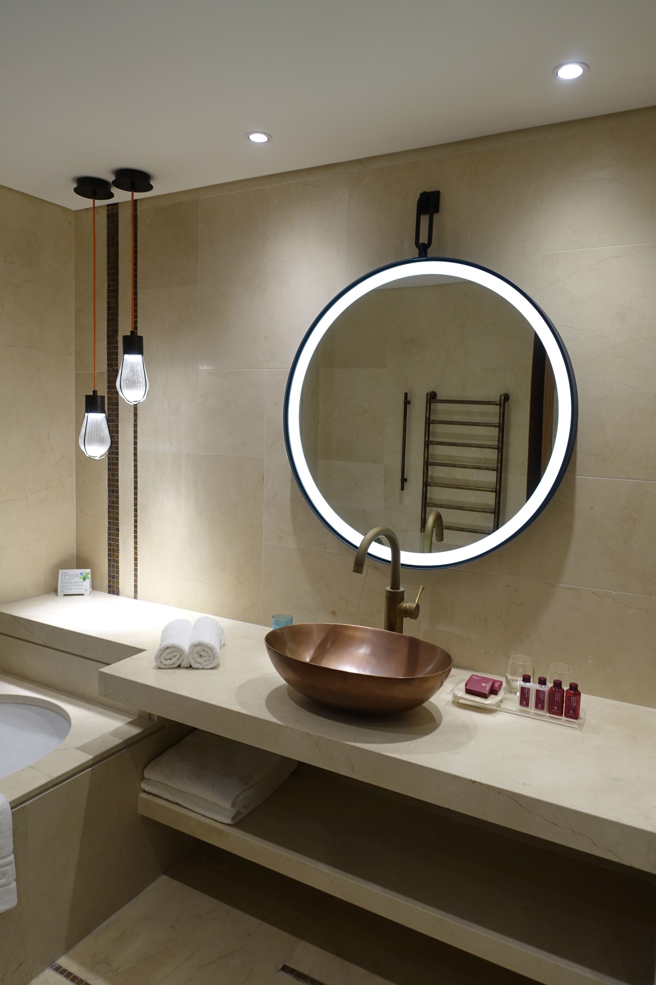 Une salle de bain moderne avec un miroir rond, un lavabo en cuivre et un porte-serviettes.