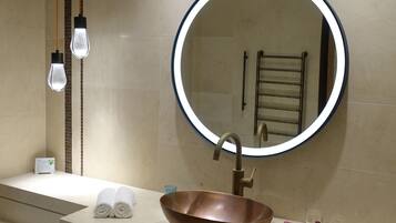 Une salle de bain moderne avec un miroir rond, un lavabo en cuivre et un porte-serviettes.