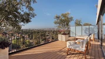 A wooden deck with outdoor furniture, a view of the city, and a glass railing.
