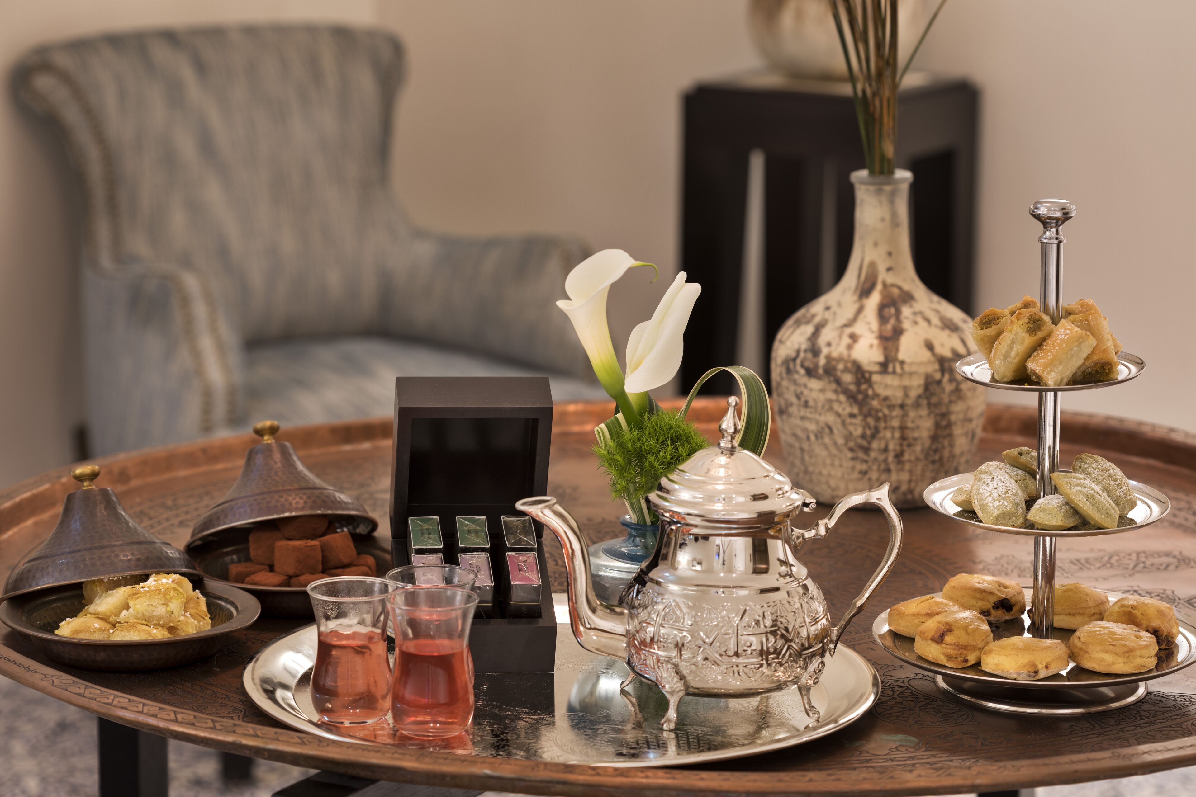 A tray with pastries, a teapot, and a glass of tea on a table.