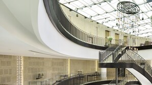 A multi-level atrium with curved staircases, glass railings, and a skylight. - Orient by Isrotel exclusive (Jerusalem)