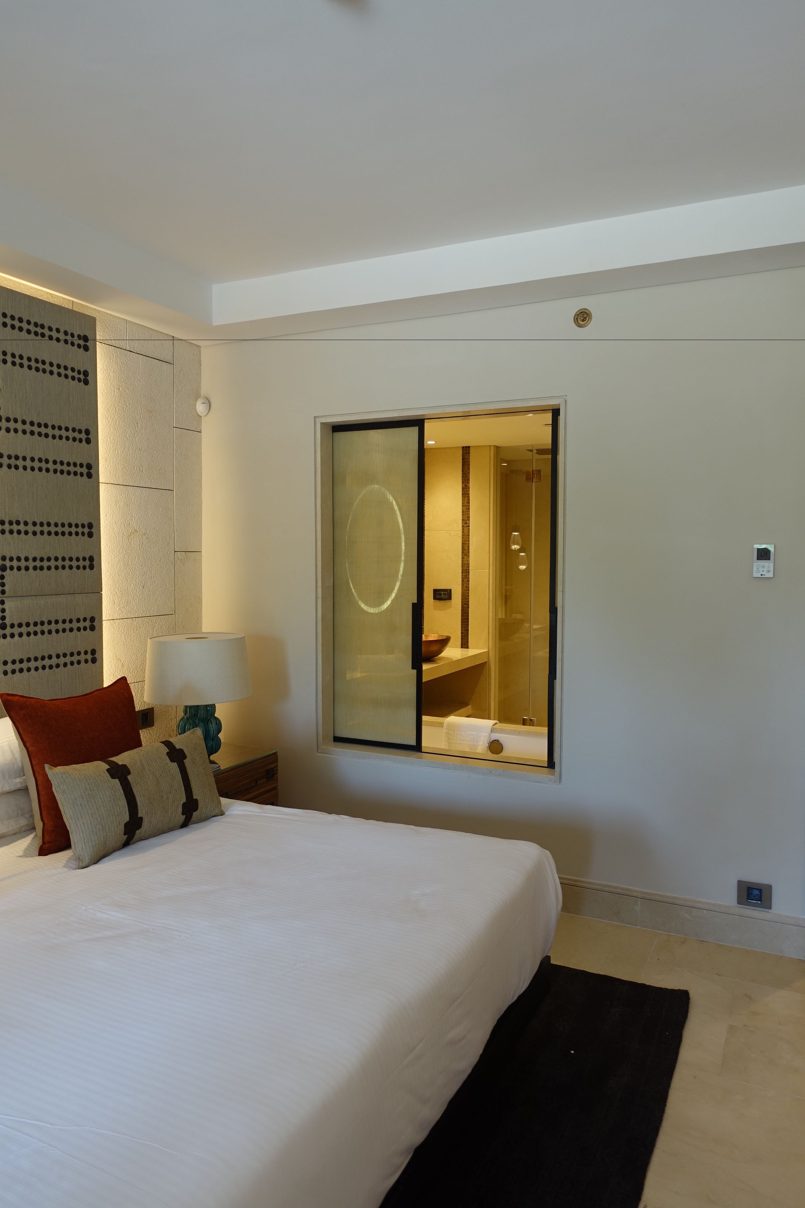 Quarto de hotel com uma cama grande, uma mesa de cabeceira com abajur, um espelho e vista para o banheiro.