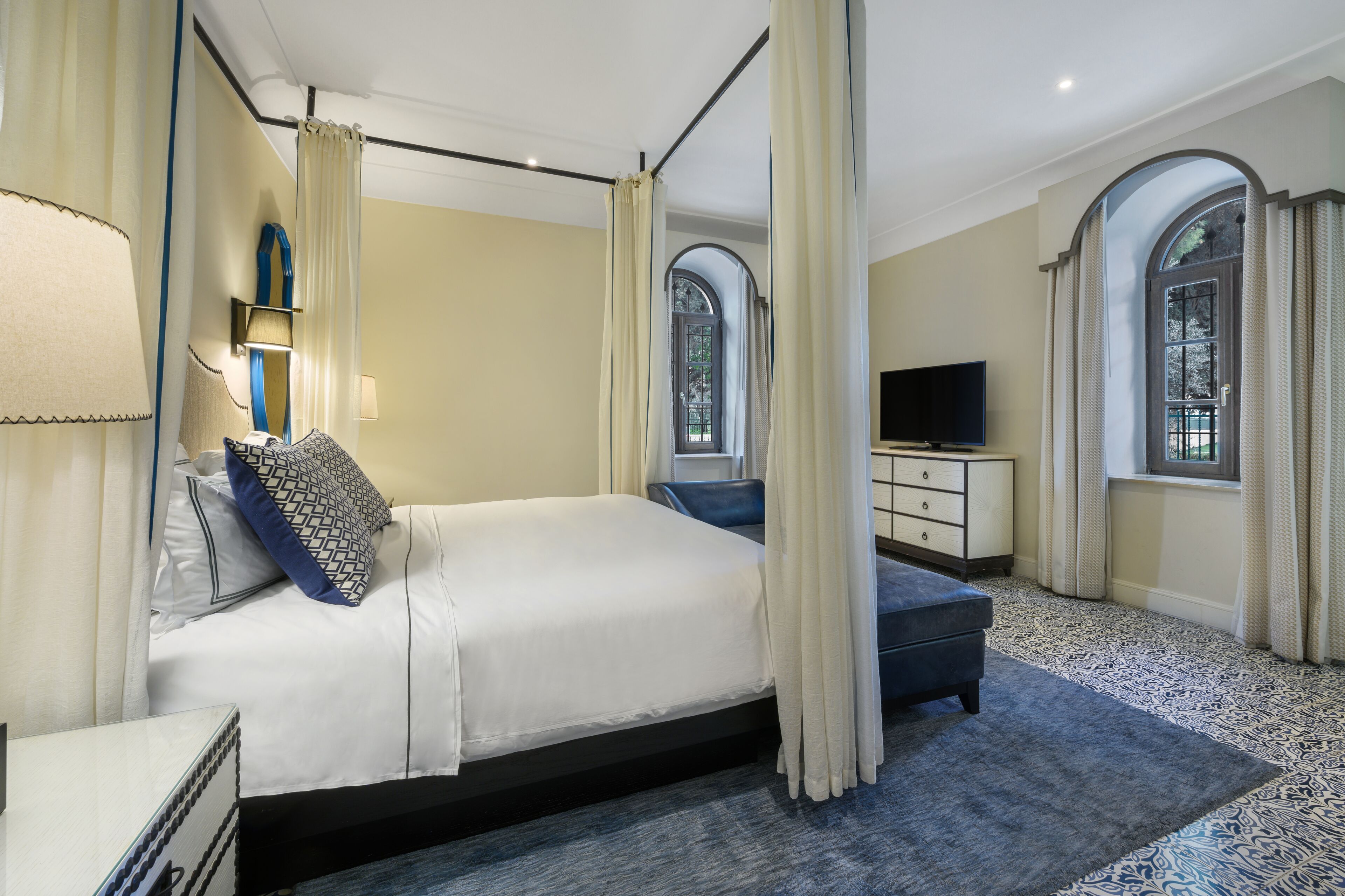 Un dormitorio con una cama grande, televisión y dos ventanas con cortinas.
