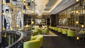 A modern hotel lobby with a central staircase, seating areas, and a bar. - Orient by Isrotel exclusive (Jerusalem)