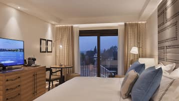 Habitación de hotel con cama, escritorio, televisor y balcón con cortinas.