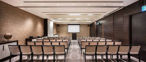A conference room with rows of chairs, a projector screen, and a patterned carpet.