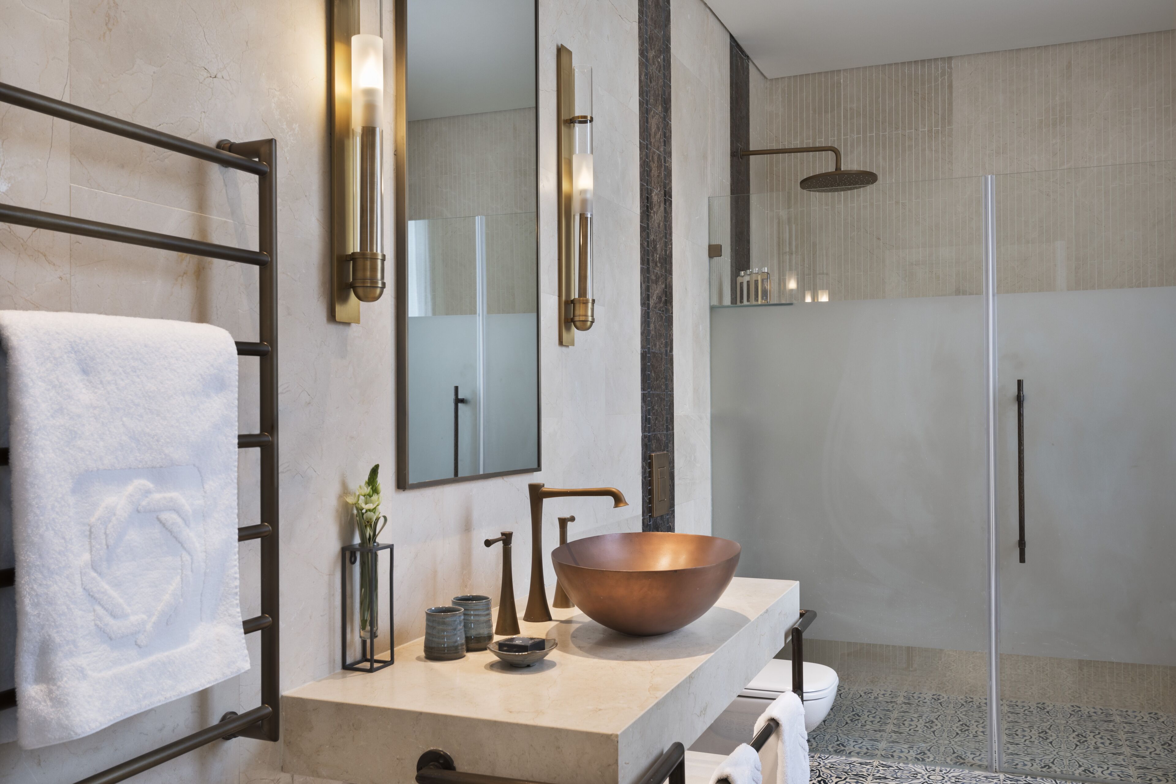 A modern bathroom with a large copper sink, a glass shower enclosure, and a towel rack with a white towel.
