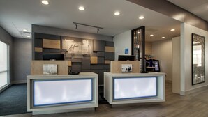 A hotel reception area with two reception desks, a wall-mounted digital screen, and a security camera.