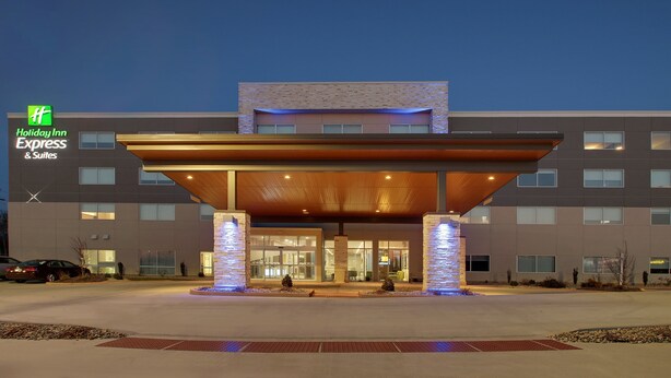 A Holiday Inn Express & Suites building with a modern design, featuring a covered entrance and illuminated pillars.