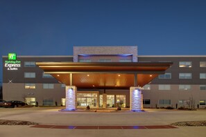 Un bâtiment de la chaîne Holiday Inn Express & Suites, doté d’un design moderne, avec une entrée abritée et des piliers illuminés.