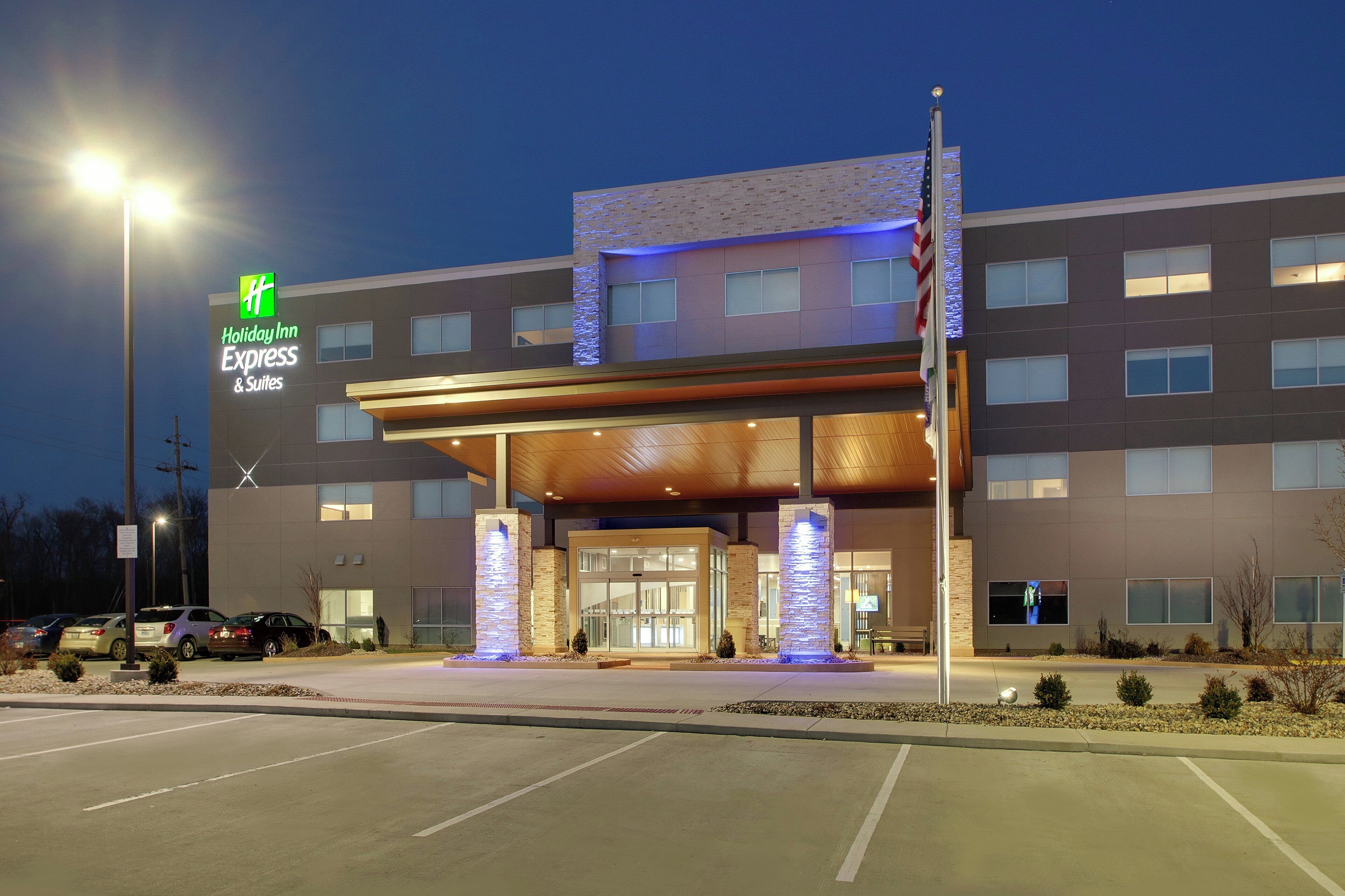 A Holiday Inn Express & Suites building with a modern design, featuring a prominent entrance with a covered walkway and stone pillars.
