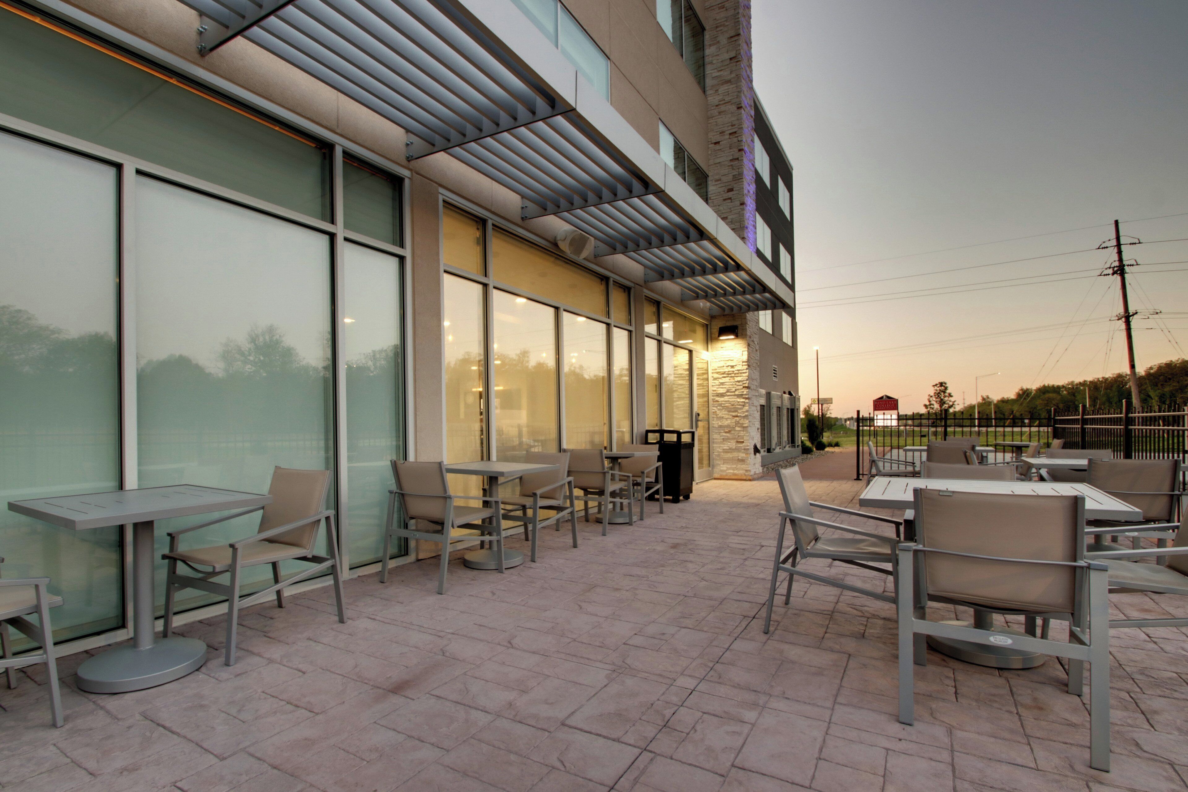 An outdoor patio area with tables and chairs, large windows, and a stone wall.
