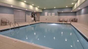 An indoor swimming pool with tiled walls, a lifeguard chair, and a pool ladder.