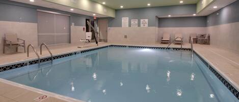 An indoor swimming pool with tiled walls, a lifeguard chair, and a pool ladder.