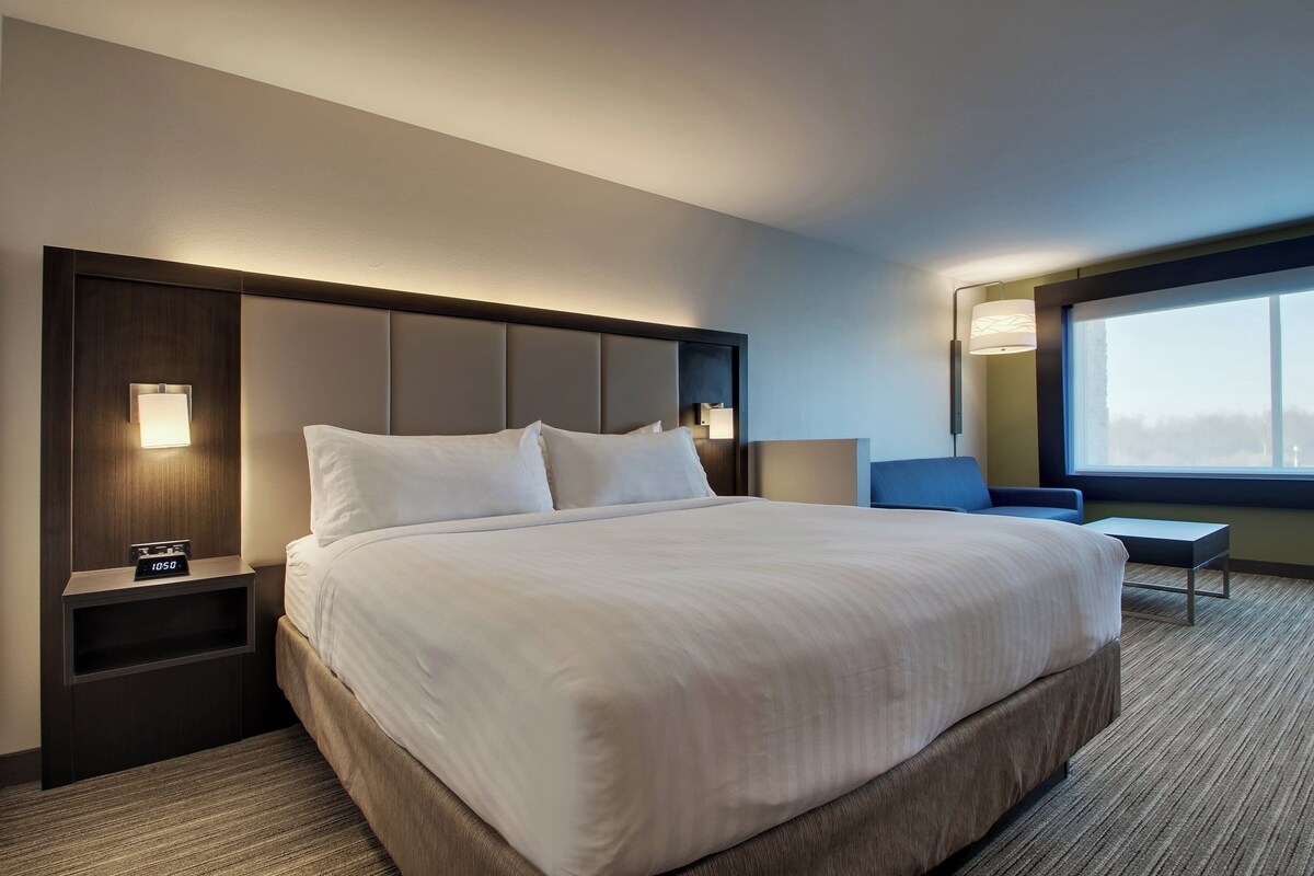 Une chambre d’hôtel avec un grand lit, des tables de chevet, une commode, un bureau et une fenêtre donnant sur un beau paysage.
