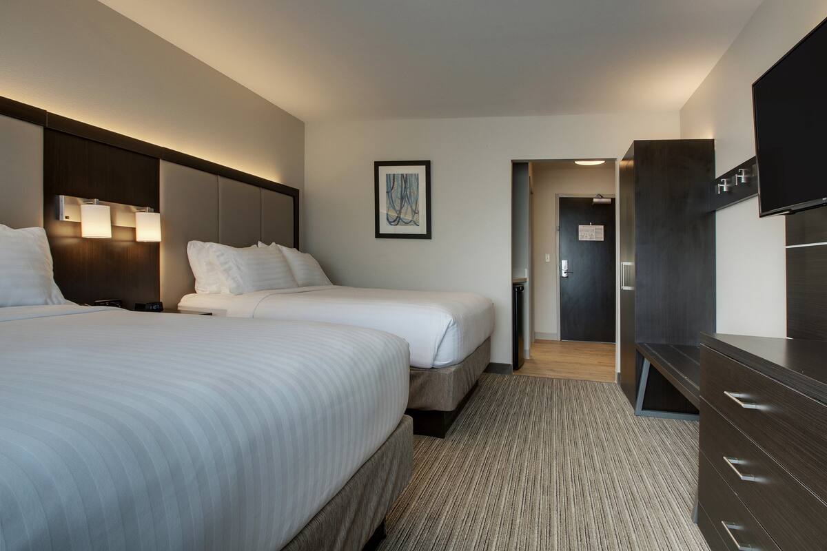 A hotel room with two beds, a flat-screen TV, a framed artwork on the wall, and a wooden floor.