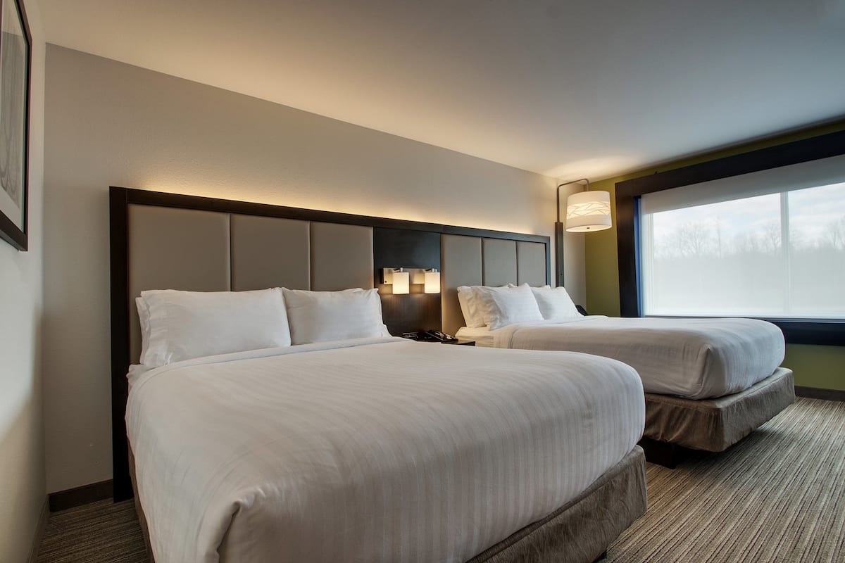 A hotel room with two beds, a headboard with integrated lighting, a nightstand, and a window with a view.