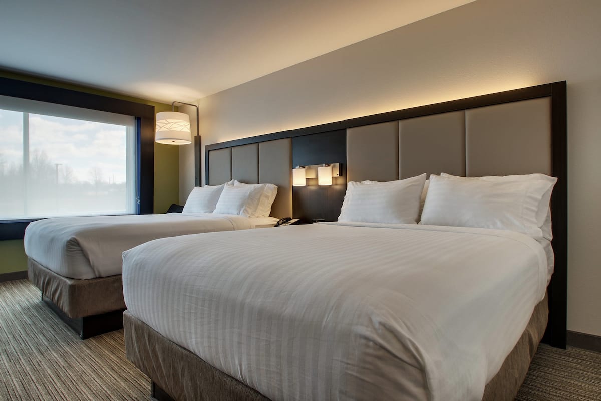 A hotel room with two beds, a large window, and a wall-mounted lamp.