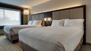 A hotel room with two beds, a large window, and a wall-mounted lamp.