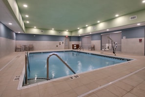 An indoor swimming pool with clear lane markings, a lifeguard chair, and a changing room area.