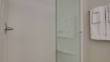 Une salle de bain moderne avec une douche à parois de verre, un mur recouvert de carreaux blancs et un porte-serviettes avec plusieurs serviettes.