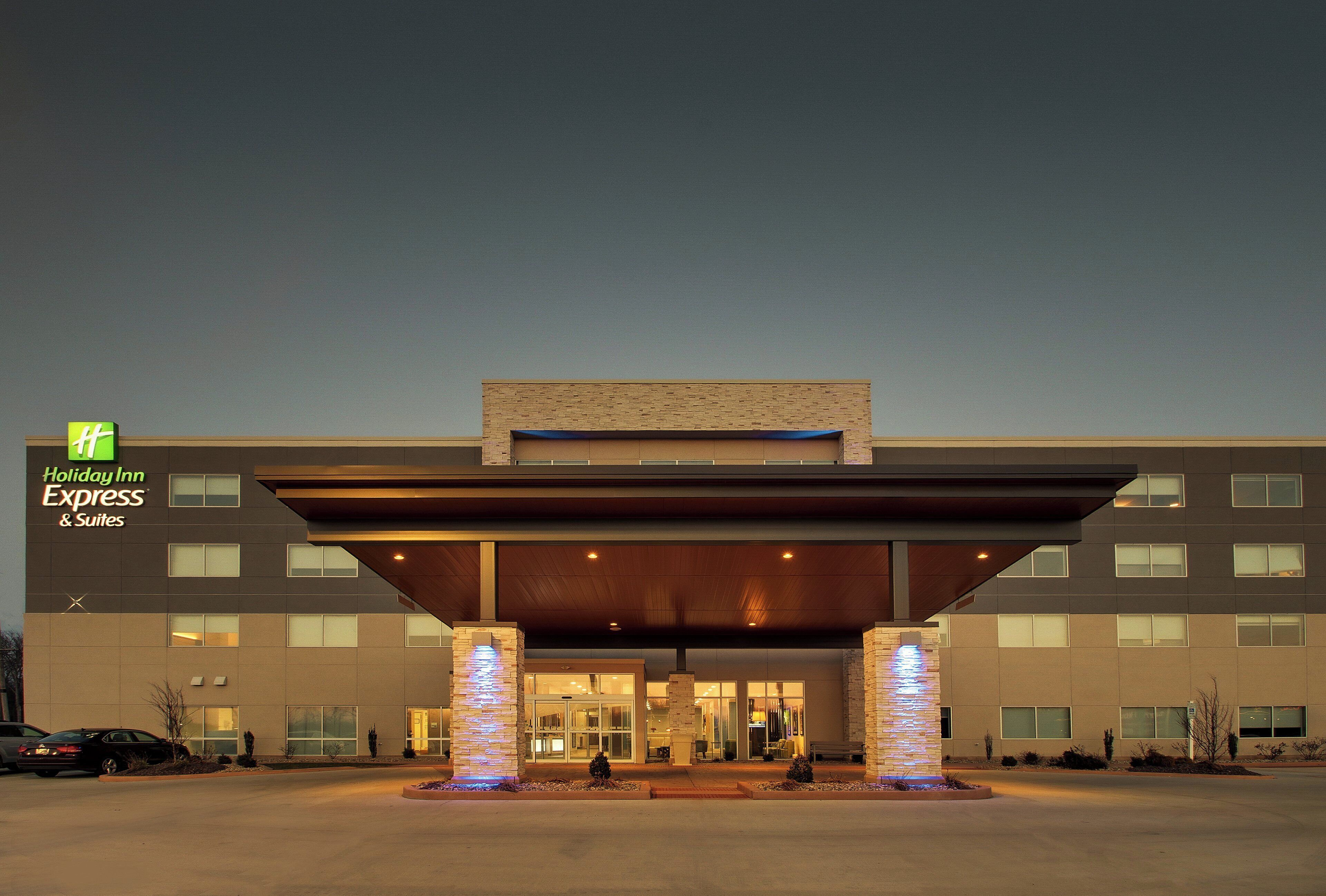 A Holiday Inn Express & Suites building with a modern entrance, large windows, and a landscaped front yard.